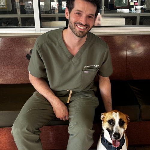 Dr. Matthew Basch in scrubs, seated with a terrier beside him.